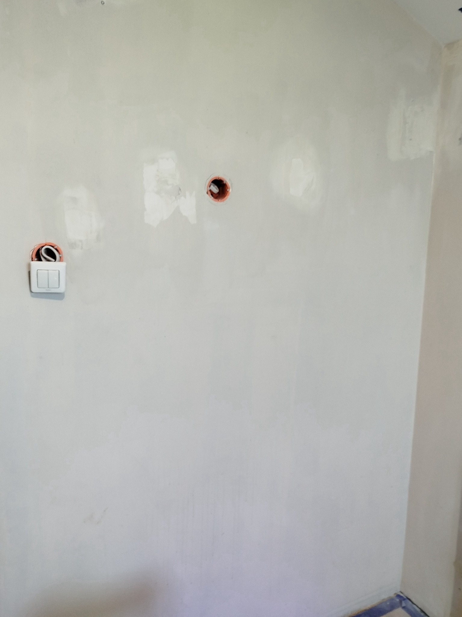 Ściana po szpachlowaniu z zamontowanym, podwójnym włącznikiem światła i puszkami elektrycznymi. Widoczne przewody.