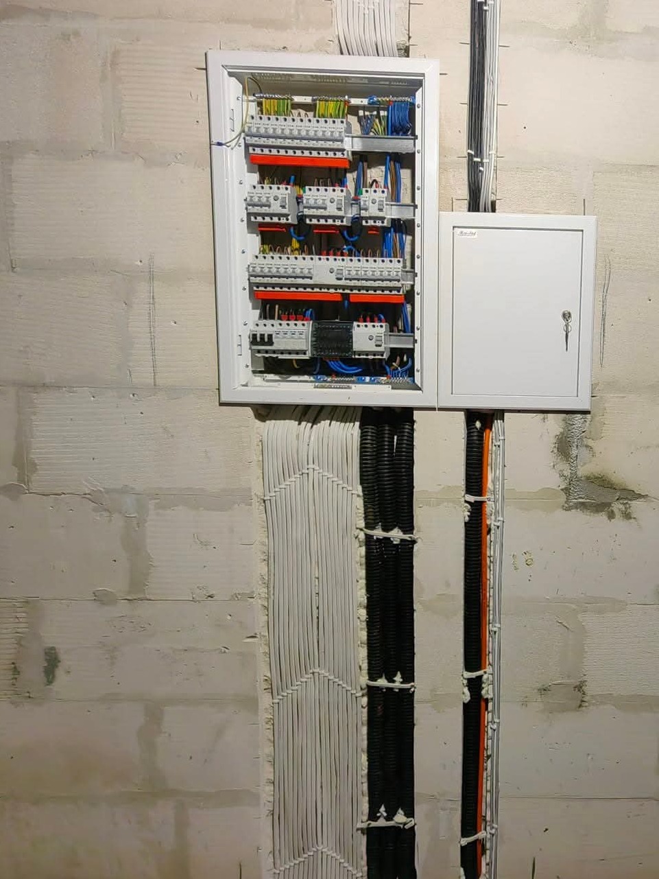 Rozdzielnia elektryczna z otwartymi drzwiczkami, widoczne zabezpieczenia i okablowanie. Kable prowadzone w ścianie, zabezpieczone pianką montażową.