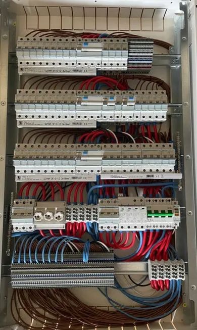 Rozdzielnica elektryczna z precyzyjnie ułożonymi przewodami w kolorach niebieskim i czerwonym, zabezpieczenia modułowe zamontowane w metalowej obudowie.