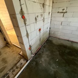 Voltex Robert Szkudlarek - Wnętrze w trakcie prac: ściany z betonu komórkowego z widocznymi przewodami elektrycznymi w peszlach i puszkami instalacyjnymi, surowa podłoga.