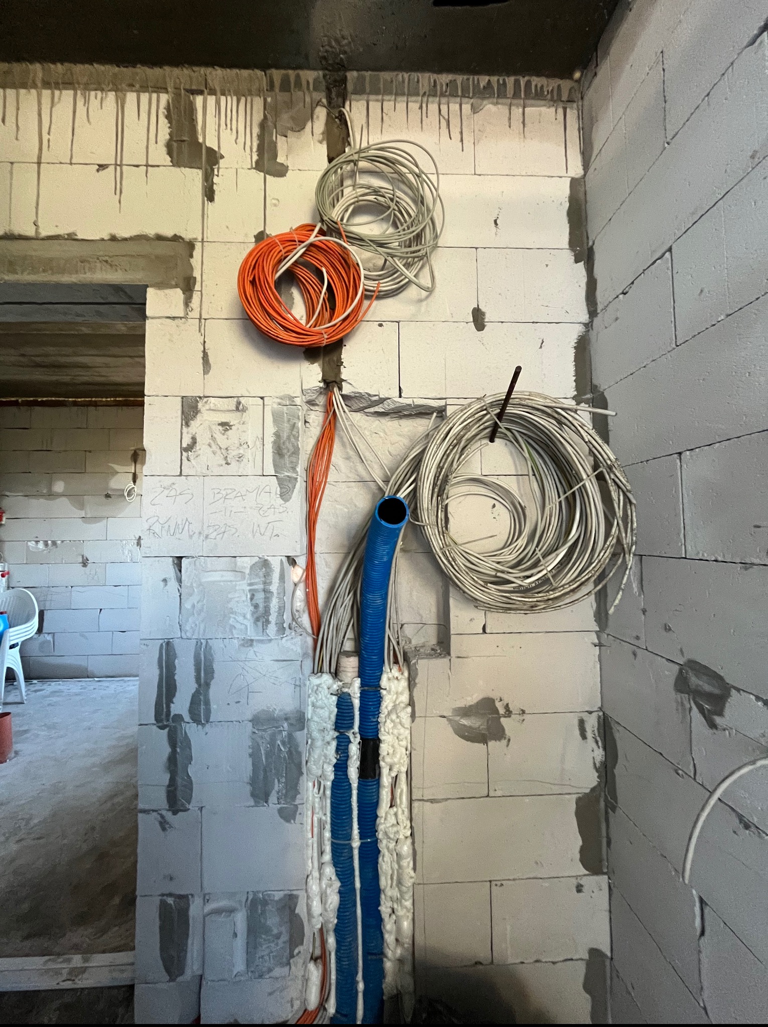 Surowe ściany z betonu komórkowego z widoczną instalacją elektryczną w peszlach, zabezpieczoną pianką montażową. Kłęby kabli w kolorach pomarańczowym i białym.
