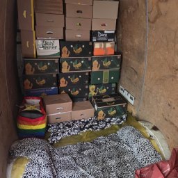 Konrad Blachaniec - Wnętrze furgonetki wypełnione kartonami, niektóre z logo 'Yellow Banana Santa Marta', oraz przedmiotami osobistymi, w tym kolorową torbą i wzorzystą pościelą.