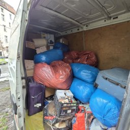 Konrad Blachaniec - Wnętrze białego busa wypełnione po brzegi workami w kolorze niebieskim i czerwonym, kartonami i walizkami podczas przeprowadzki. Widok z zewnątrz na załadowany pojazd.