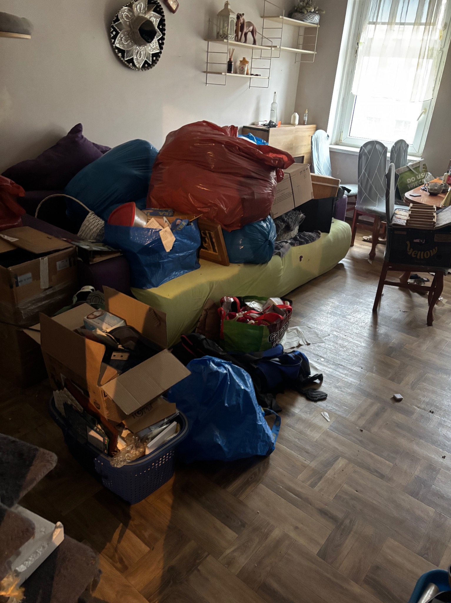 Pokój przed przeprowadzką: kartony, worki z rzeczami, meble. Chaos przed transportem, widok na podłogę i część wyposażenia.