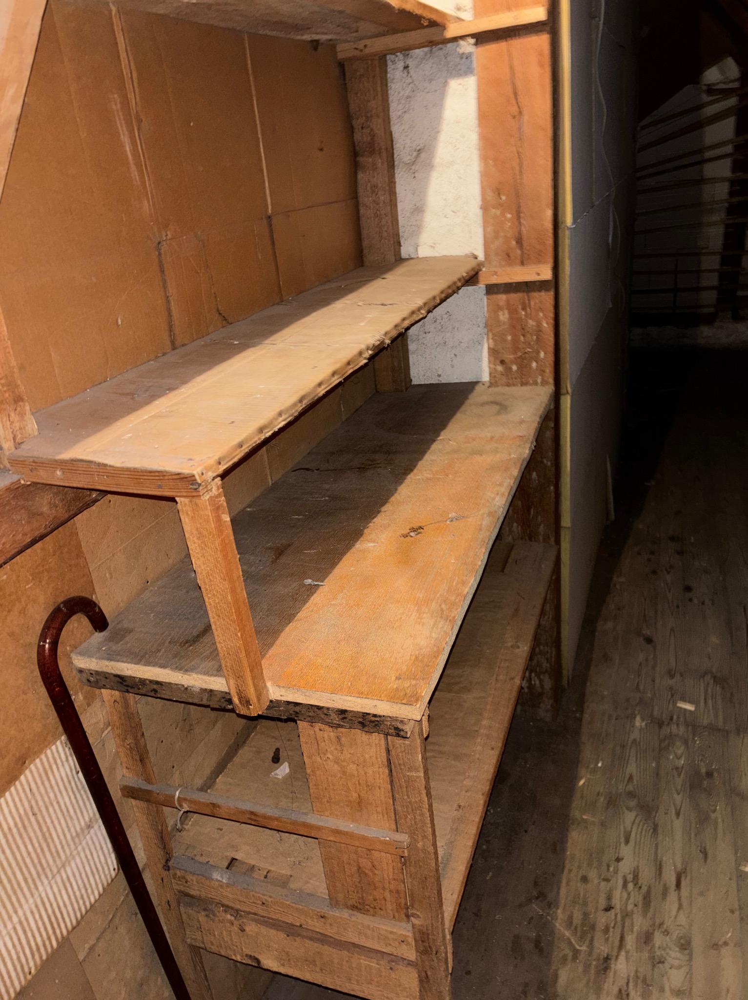 Drewniane, prowizoryczne półki w trakcie rozbiórki, widoczne elementy konstrukcyjne i fragment podłogi. W tle ściana z widocznymi śladami demontażu.