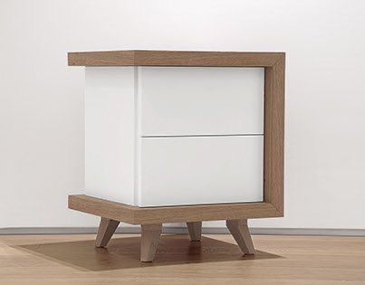 Biała szafka nocna z dwoma szufladami, obudowana ramą z jasnego drewna, na niskich nóżkach, w minimalistycznym stylu, na tle białej ściany i drewnianej podłogi.