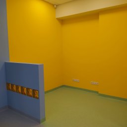 BET-MAR Beata Stępień - Pomalowane na żółto ściany w pomieszczeniu z zieloną podłogą i niebieskim elementem architektonicznym z wieszakami. Widoczne gniazdka elektryczne.