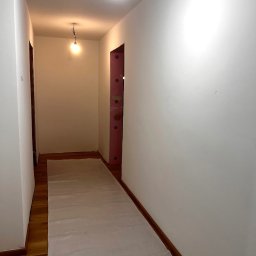 Tomasz Skwirzynski - Korytarz po świeżym malowaniu na biało, zabezpieczona podłoga, widoczne ślady po remoncie. Oświetlenie sufitowe. Ujęcie z dołu, perspektywa wnętrza.