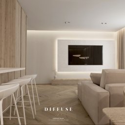 Diffuse Design Studio Dominika Wasik - Jasne, minimalistyczne wnętrze z drewnianą podłogą w jodełkę, beżową sofą i barkiem z białymi hokerami. Telewizor w ozdobnej ramie z podświetleniem LED.