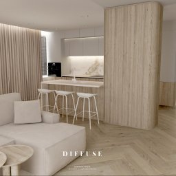 Diffuse Design Studio Dominika Wasik - Jasne wnętrze z drewnianą zabudową: kuchnia z wyspą i białymi hokerami, beżowa sofa i parkiet w jodełkę. Minimalistyczny design z akcentami drewna.