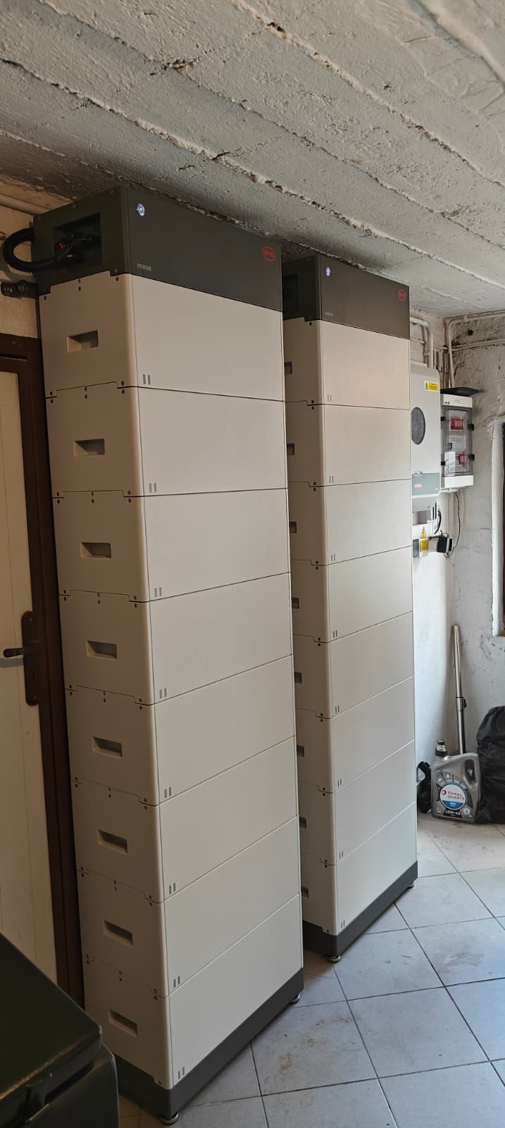 Dwa modułowe magazyny energii BYD w piwnicy z widoczną instalacją elektryczną i betonowym sufitem. Realizacja instalacji magazynów energii.