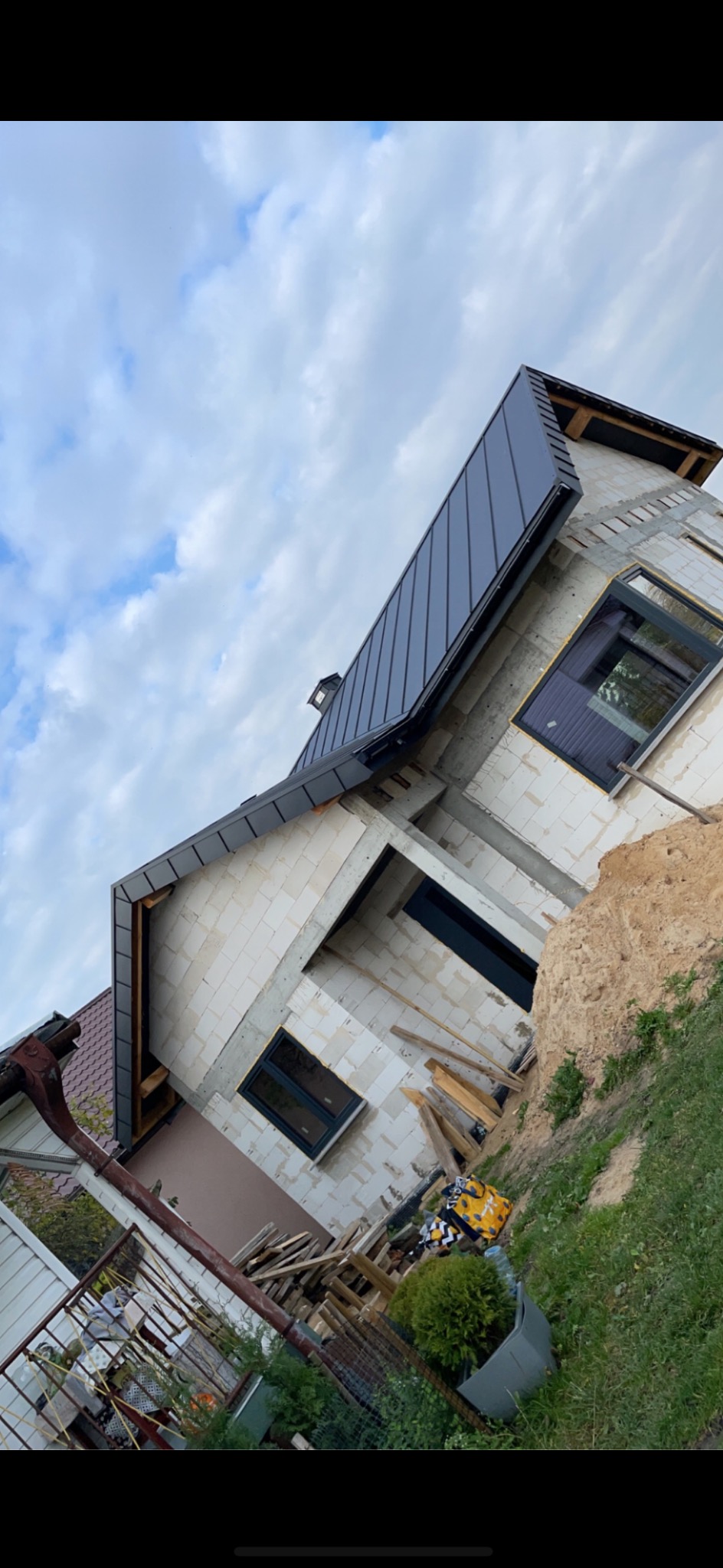 Dom w trakcie budowy z nowym, grafitowym dachem z blachy na rąbek stojący. Widoczne okna z czarną stolarką i białe bloczki betonu komórkowego.