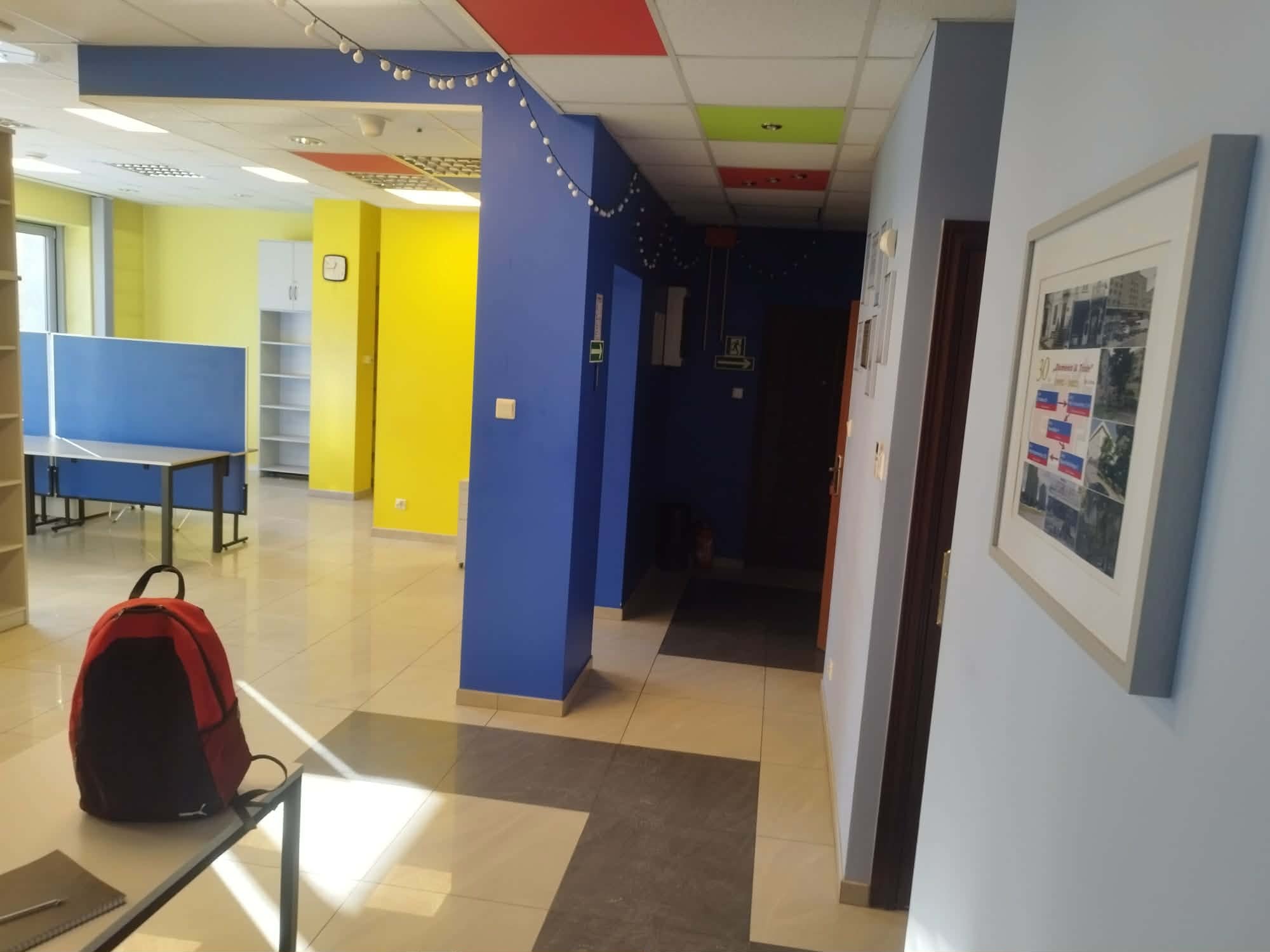 Wnętrze biura po malowaniu: ściany w odcieniach żółci, błękitu i granatu, oświetlenie sufitowe, widoczny fragment biurka i krzesła. Dekoracja w postaci lampek.