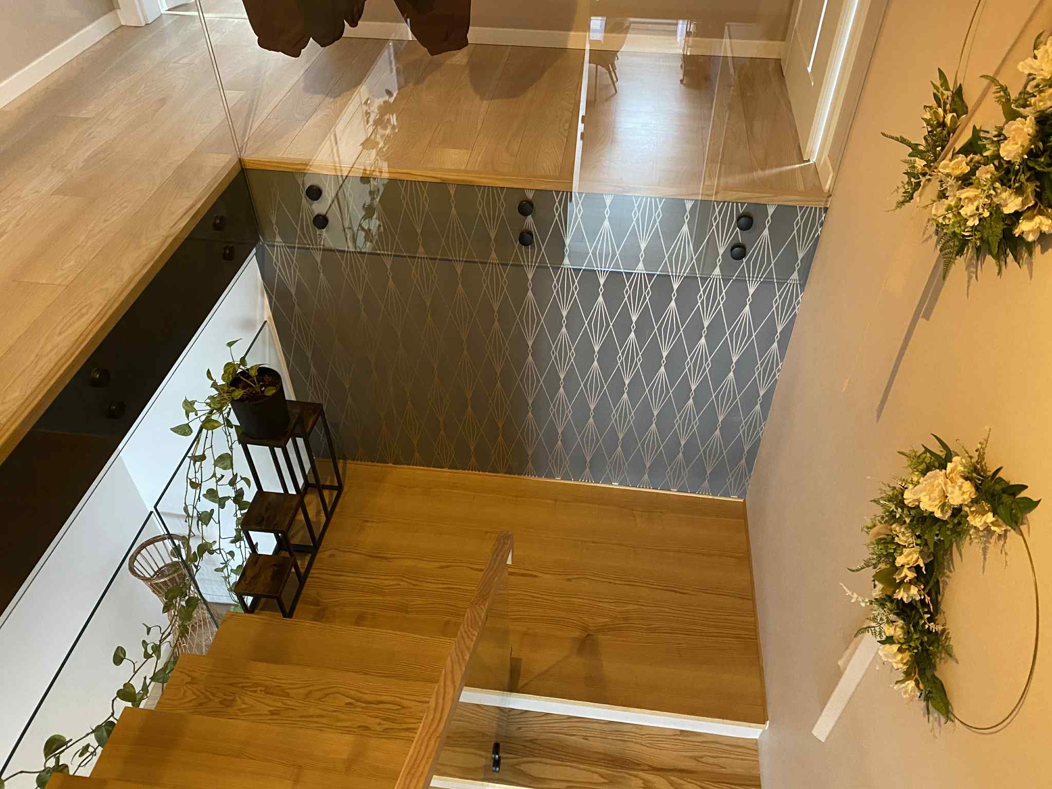 Nowoczesne schody drewniane z balustradą szklaną, widok z góry. Dekoracyjna tapeta w geometryczne wzory i kwiatowe dekoracje ścienne.