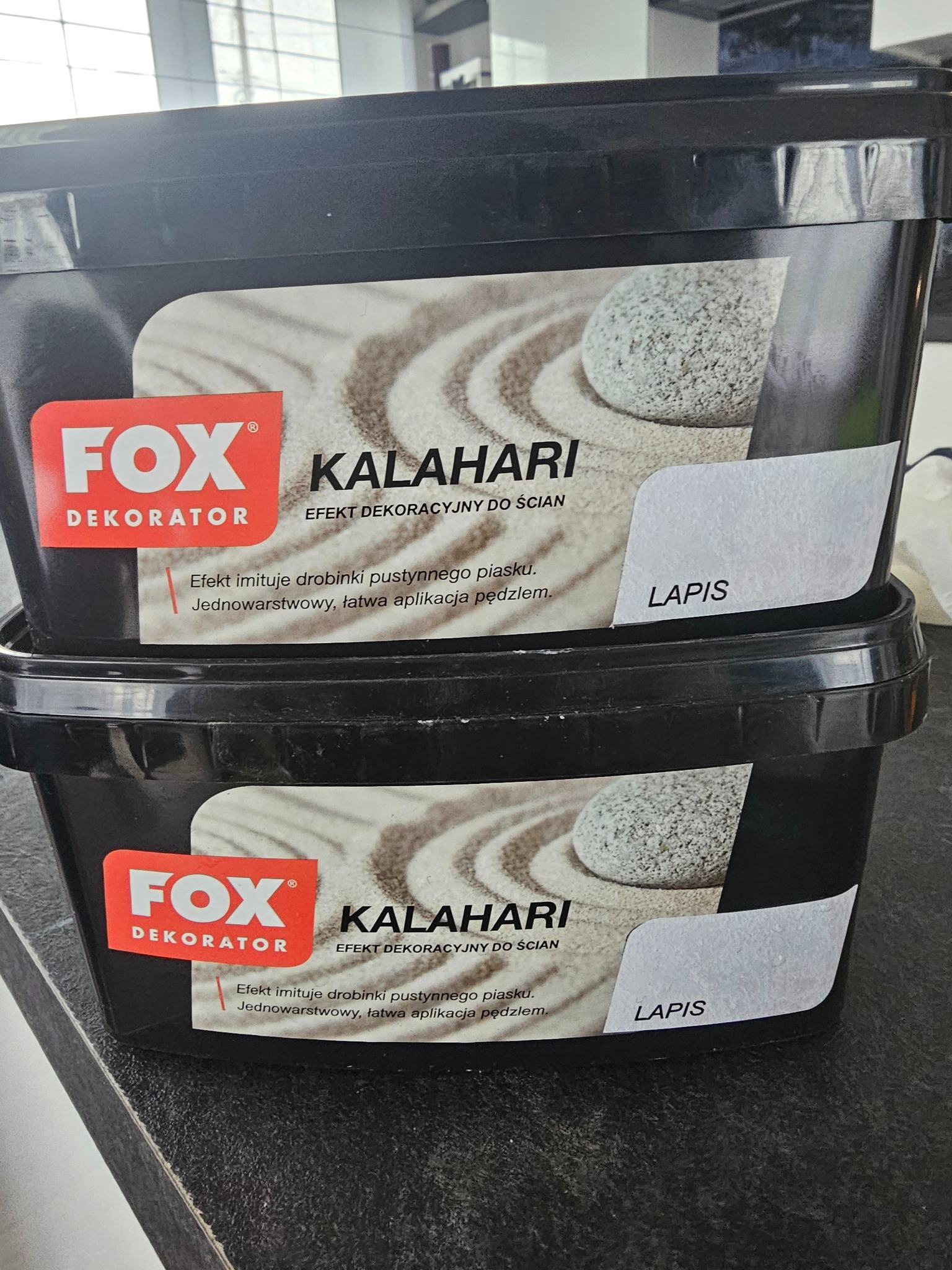 Dwa czarne pojemniki z efektem dekoracyjnym do ścian Fox Dekorator Kalahari Lapis, imitującym pustynny piasek, ustawione jeden na drugim.