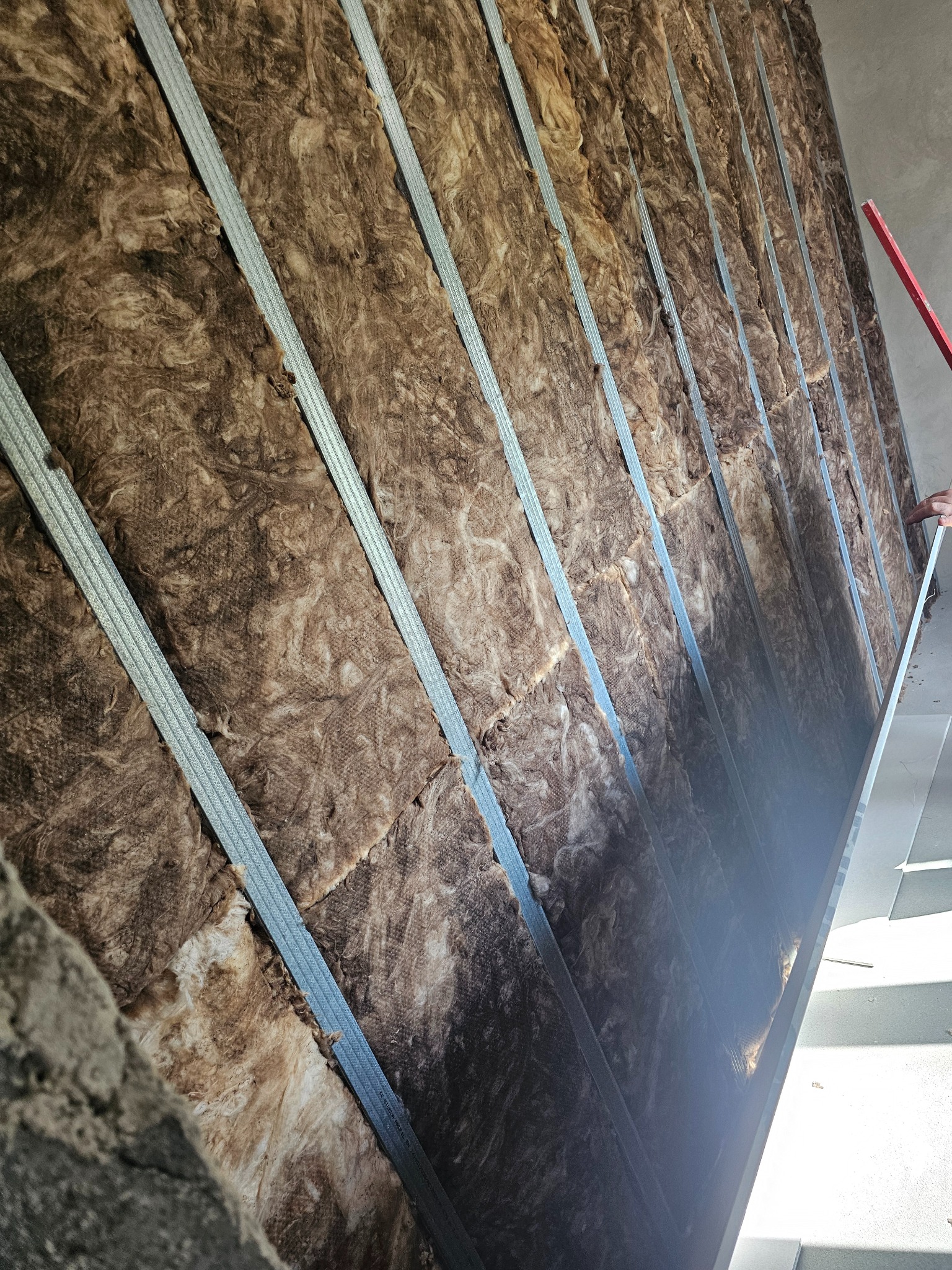 Izolacja ścian wełną mineralną, widoczne metalowe profile konstrukcyjne. Prace wykończeniowe w trakcie montażu. Ujęcie z dołu, ukazujące strukturę materiałów.