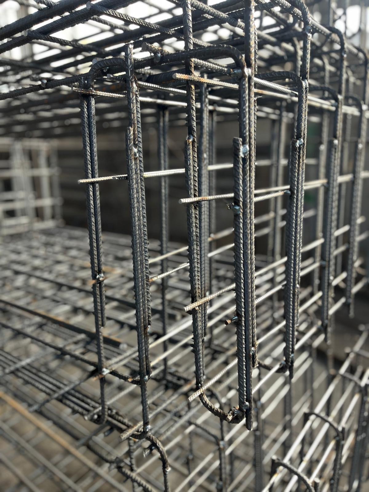 Siatka zbrojeniowa z żebrowanych prętów, połączonych drutem, tworząca szkielet konstrukcji. Widoczne detale łączeń i faktura prętów w surowym oświetleniu.