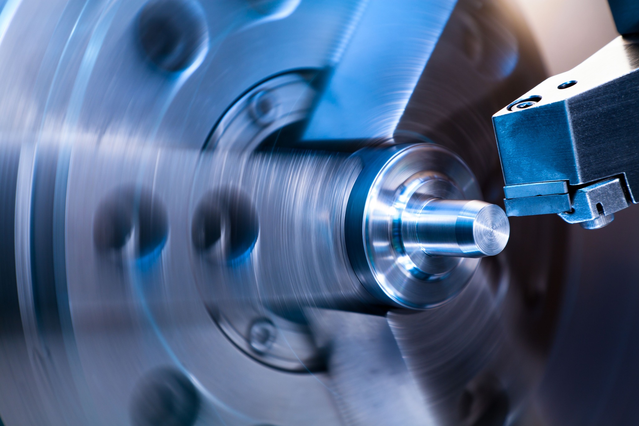 Dynamiczne ujęcie procesu toczenia metalu w Raszkowie. Wrzeciono w ruchu, narzędzie skrawające w akcji, detale obróbki widoczne. Chłodne, niebieskie oświetlenie.