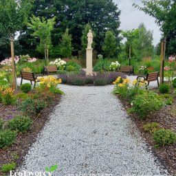 Robert Pilecki Consulting - Ogród z kamienną ścieżką, rzeźbą i ławkami. Rabaty kwiatowe z żółtymi i fioletowymi kwiatami. Widoczne drzewa i krzewy. Całość utrzymana w spokojnej, parkowej stylistyce.