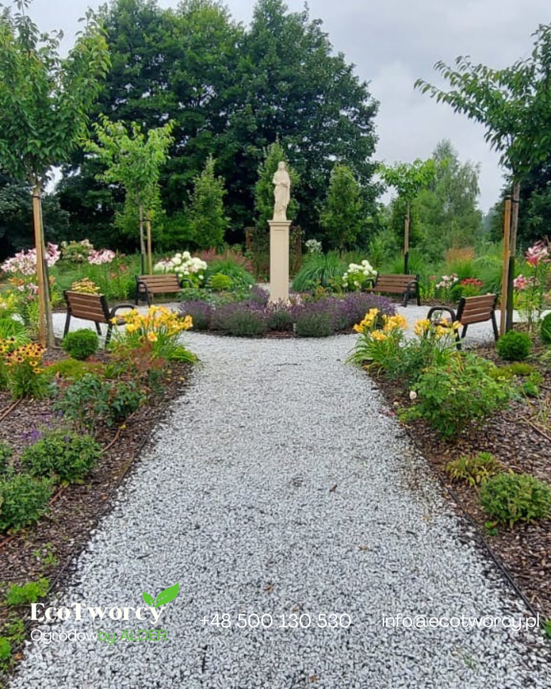 Ogród z kamienną ścieżką, rzeźbą i ławkami. Rabaty kwiatowe z żółtymi i fioletowymi kwiatami. Widoczne drzewa i krzewy. Całość utrzymana w spokojnej, parkowej stylistyce.