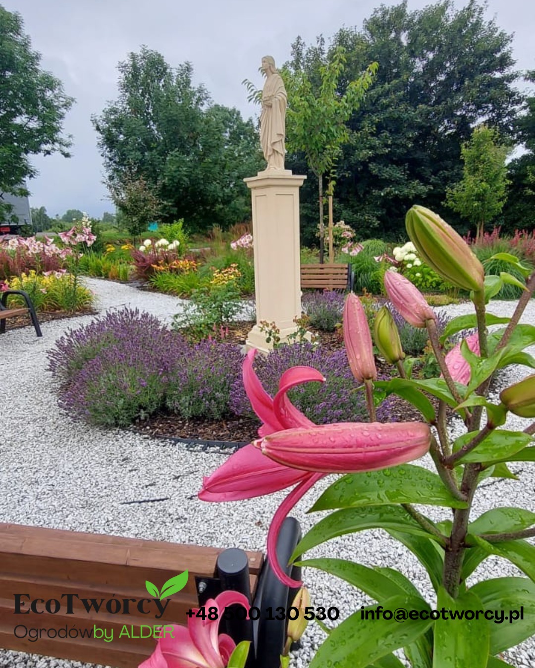 Ogród z rzeźbą na postumencie, ścieżką z białego żwiru, rabatami kwiatowymi i ławkami. W pierwszym planie lilia z kroplami deszczu. Projekt i realizacja ogrodu.