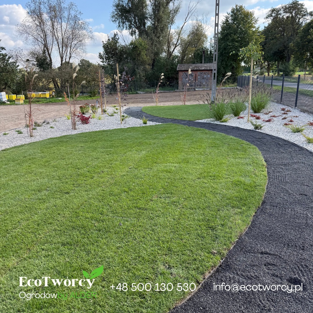 Estetyczny ogród z równo przystrzyżonym trawnikiem, ścieżką z czarnego grysu i rabatami z białego kamienia oraz roślin ozdobnych. W tle widoczne ule.