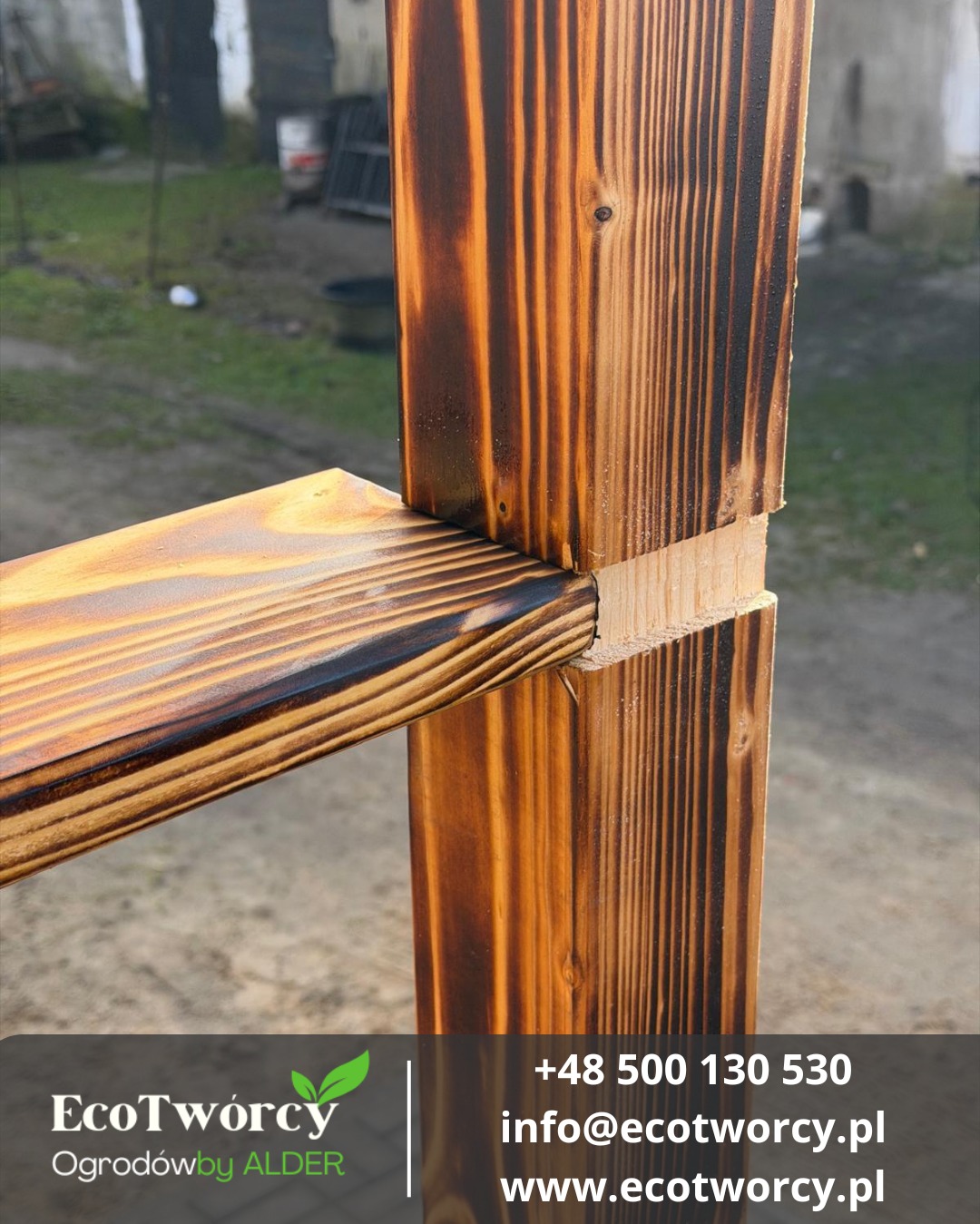 Fragment konstrukcji z opalanych desek, prawdopodobnie elementu ogrodzenia lub tarasu. Widoczne połączenie desek na zewnątrz, z wyraźnym rysunkiem słojów drewna.