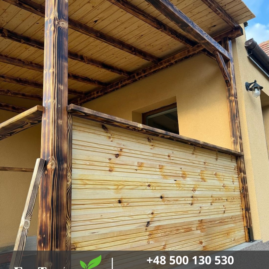 Drewniana pergola z palonego drewna, jasne deski, widok z dołu, żółta ściana budynku w tle, oświetlenie zewnętrzne, unikalne wykończenie.