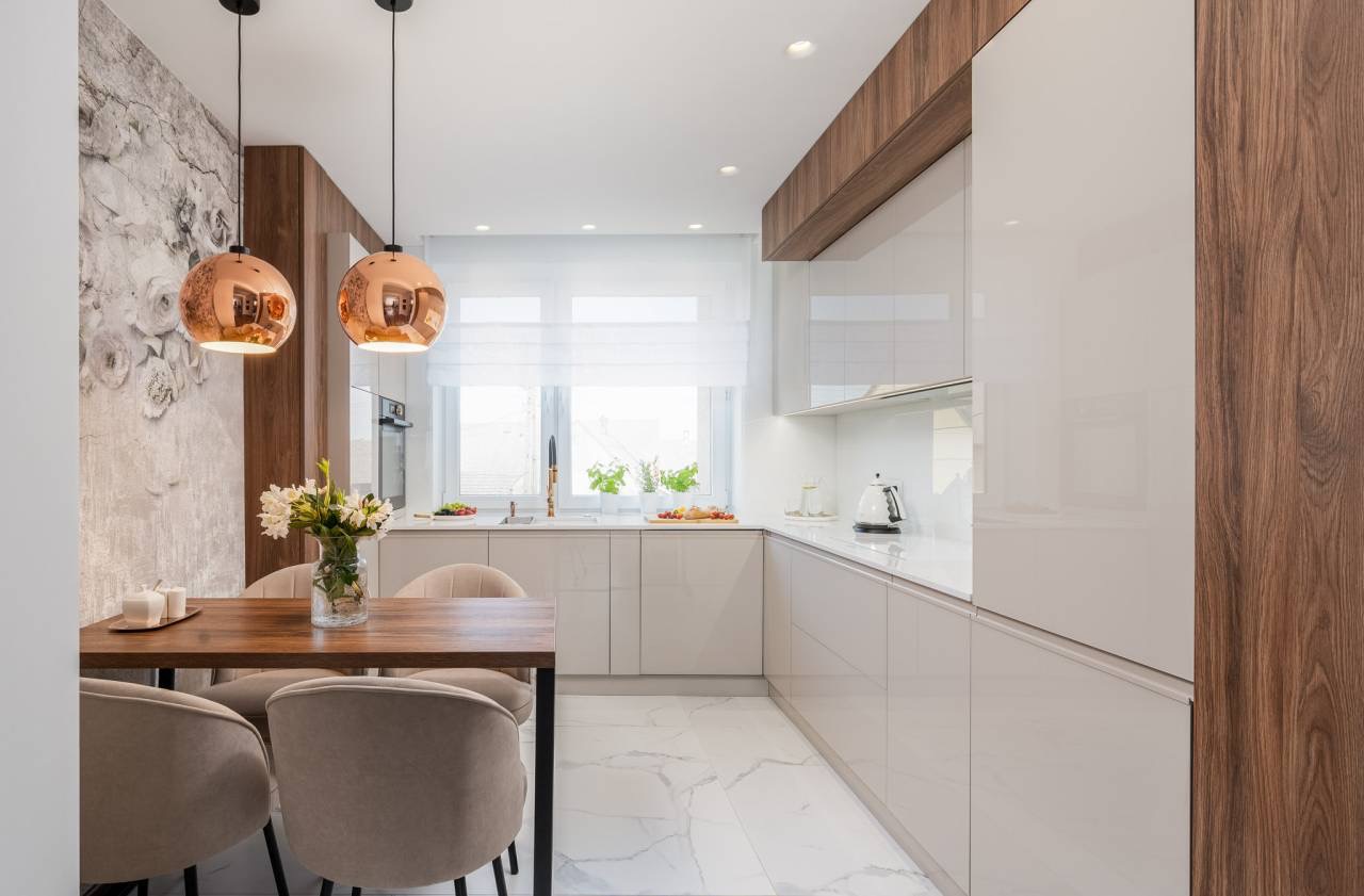 Jasna kuchnia z marmurową podłogą, drewnianymi akcentami i miedzianymi lampami. Stół z kwiatami i krzesłami dodaje przytulności. Nowoczesny design.