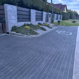 Igor Kempa - Ułożona, ciemnoszara kostka brukowa z jasnymi fugami, tworząca wzór. W tle nowoczesne ogrodzenie z elementami betonowymi i zielenią.