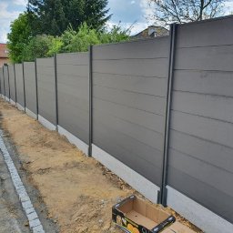 Krak Fence Sp. Z.O.O - Nowoczesne ogrodzenie panelowe w odcieniach szarości, z widoczną podmurówką i elementami montażowymi. Ujęcie z perspektywy ziemi, podkreślające długość i solidność konstrukcji.