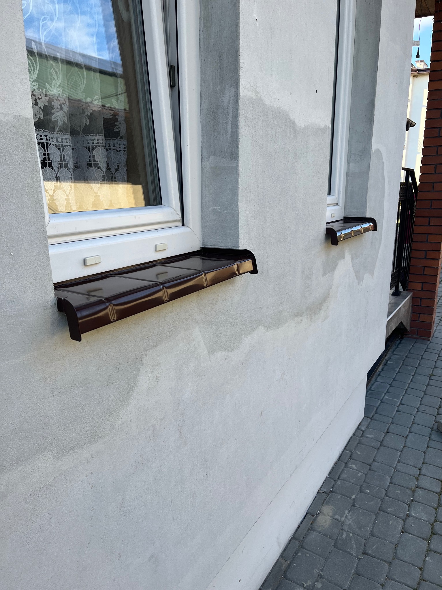 Elewacja budynku po szpachlowaniu z zamontowanymi, brązowymi parapetami zewnętrznymi. Widoczne ślady po wcześniejszych pracach przygotowawczych.