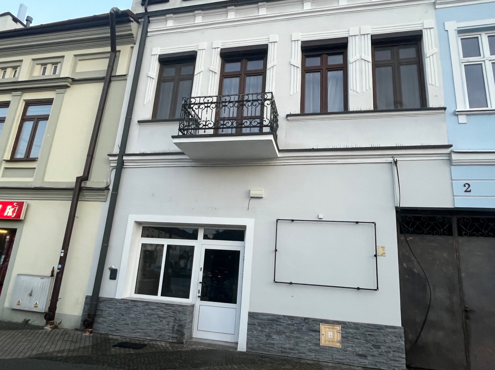 Odnowiona fasada kamienicy z balkonem i nową stolarką okienną, widoczny fragment chodnika i sąsiednich budynków. Detale architektoniczne podkreślone.