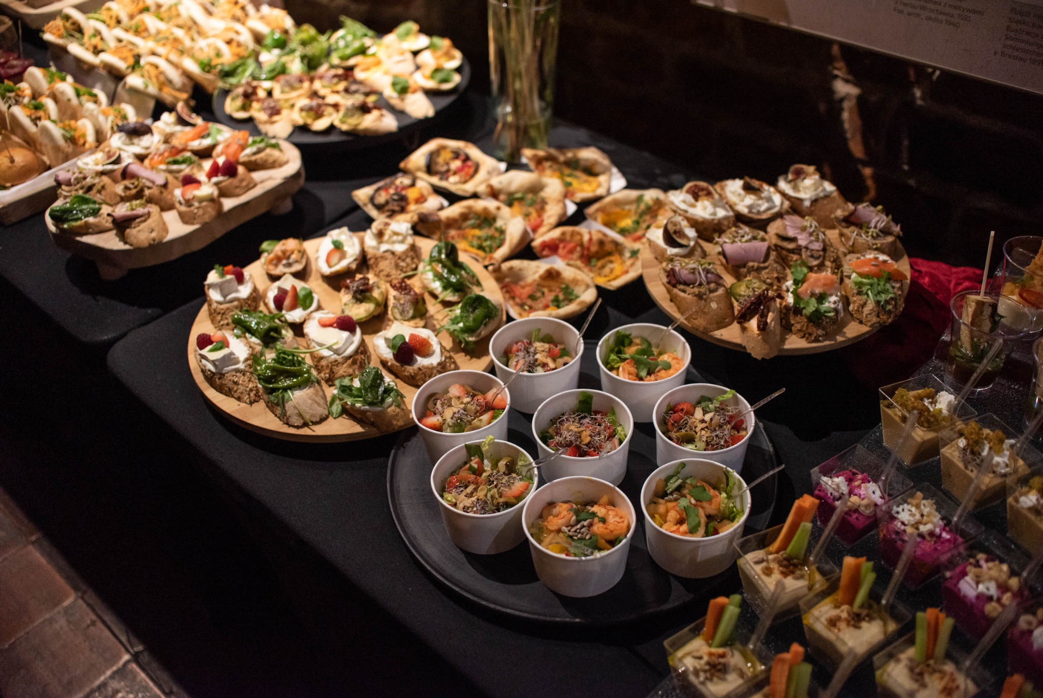 Bogato zastawiony stół cateringowy z różnorodnymi przekąskami: kanapeczki, sałatki w kubeczkach i desery w małych pojemnikach, idealne na eleganckie przyjęcie.