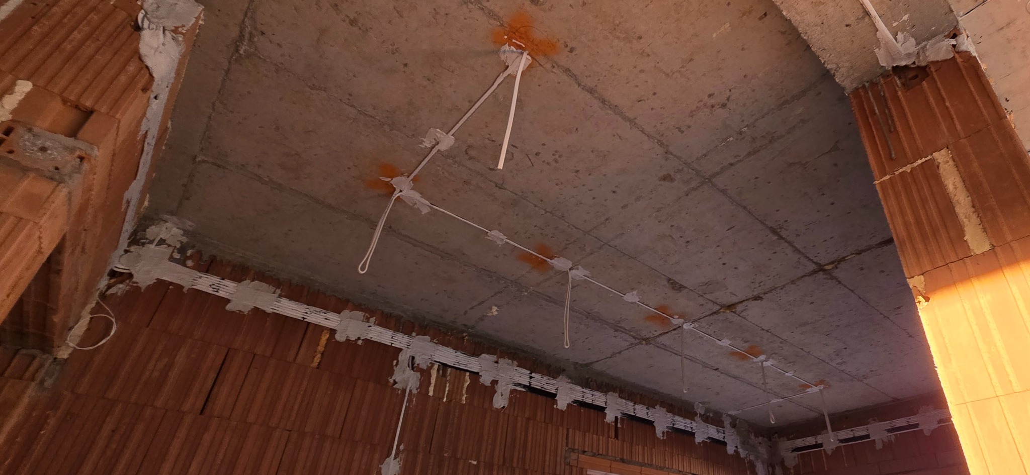 Rozprowadzone przewody elektryczne pod sufitem w surowym wnętrzu w Głogoczowie. Widoczne kable i punkty mocowania, przygotowane do montażu oświetlenia.