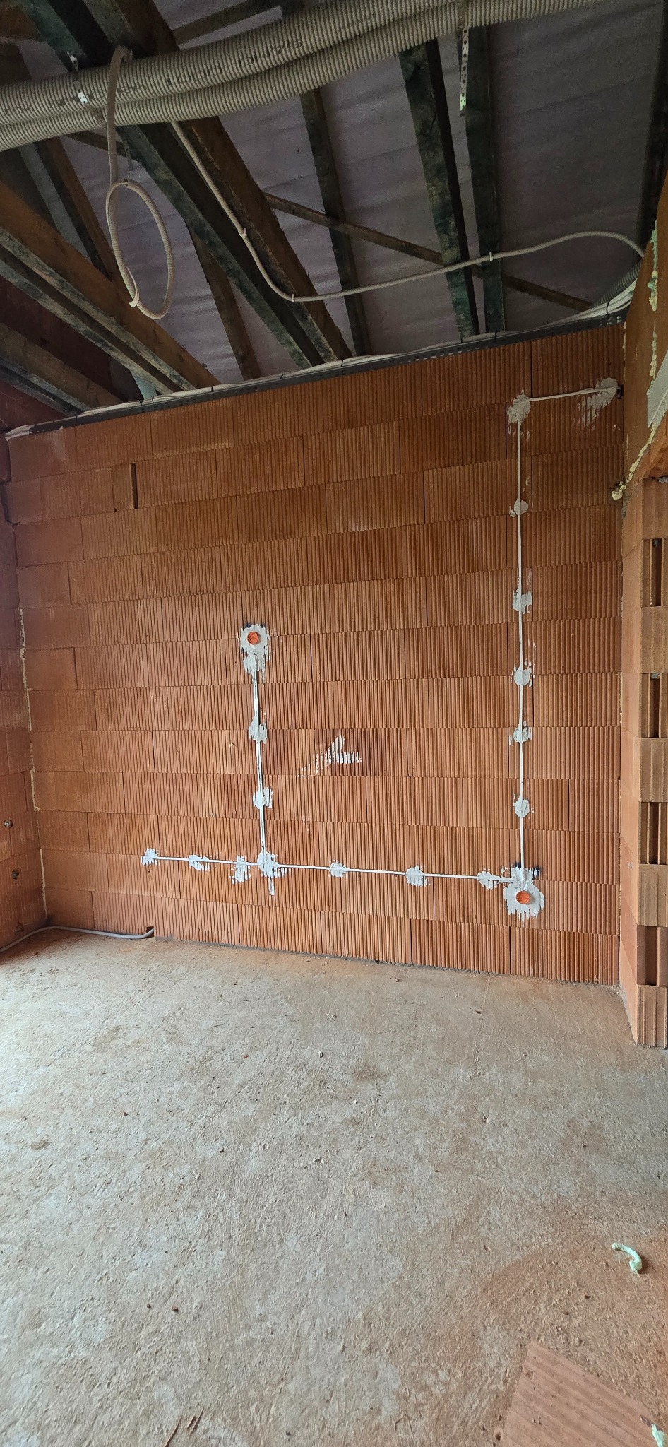 Ściana z pustaków z rozprowadzoną instalacją elektryczną. Widoczne kable i puszki podtynkowe. Na suficie rury karbowane. Surowy stan budynku.