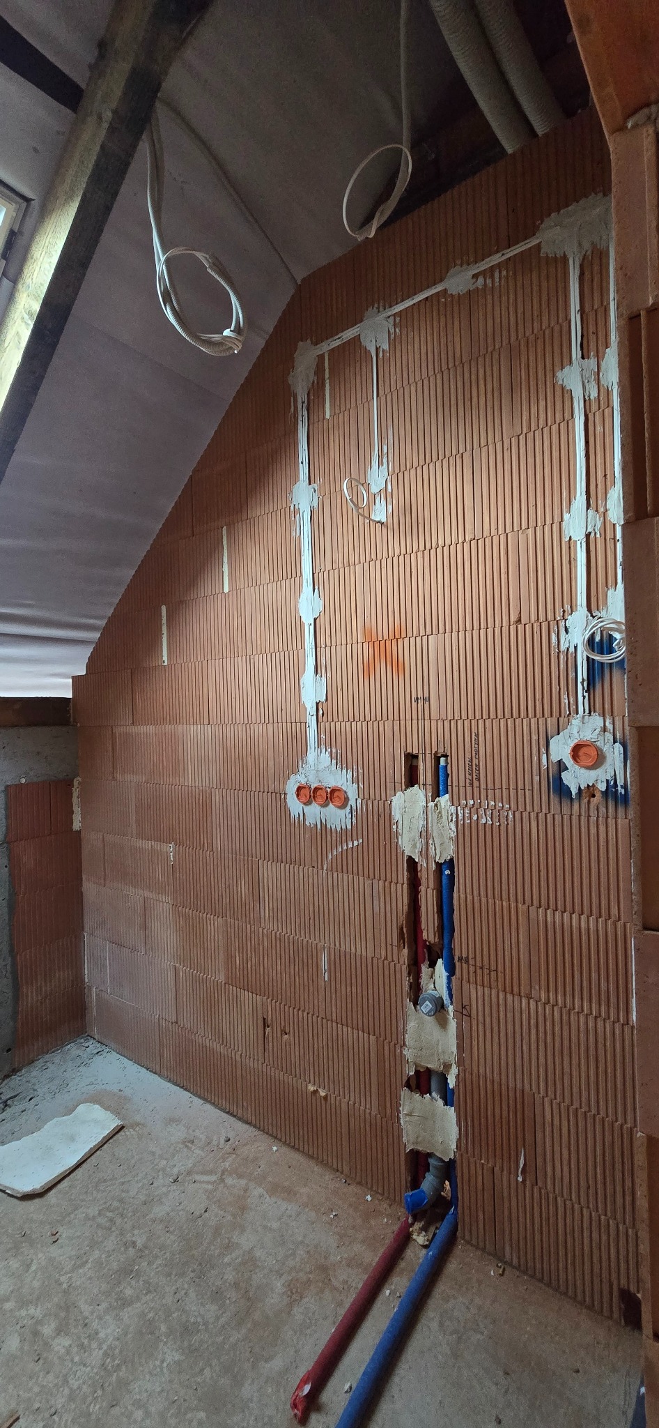 Instalacja elektryczna w bruzdach ściany z pustaków ceramicznych. Widoczne kable w peszlach, puszki pod gniazdka i rury instalacji wodnej. Prace w trakcie realizacji.