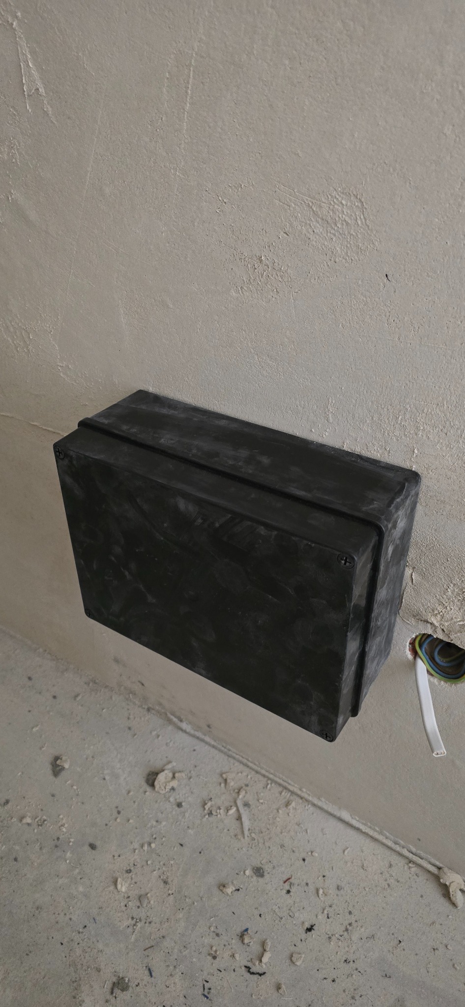 Czarna skrzynka instalacyjna na ścianie, z widocznymi przewodami. Estetyczne ukrycie sterownika LED i zasilacza w pomieszczeniu pod schodami. Surowe wykończenie wnętrza.