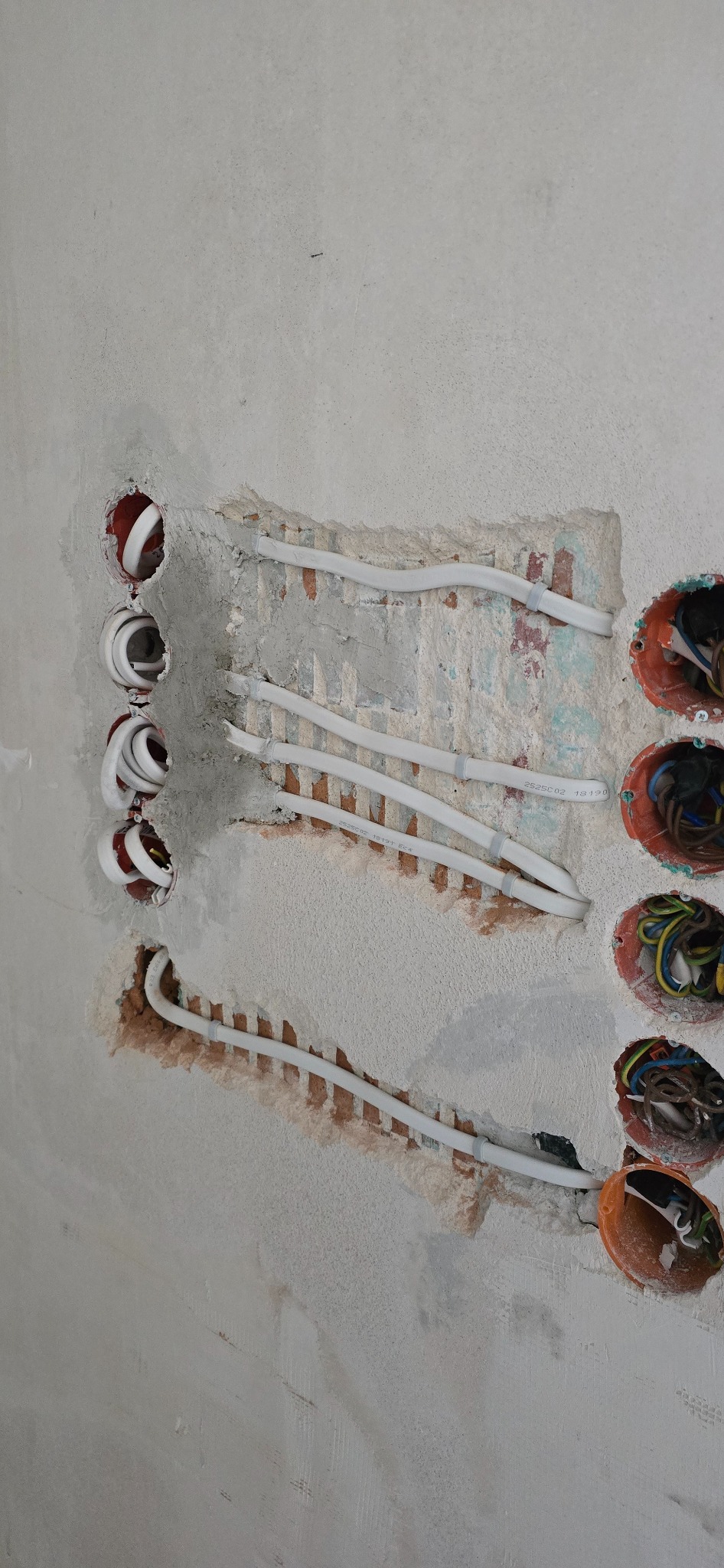 Białe kable elektryczne prowadzone w ścianie, widoczne puszki instalacyjne z przewodami. Etap prac instalacyjnych wewnątrz budynku, przed wykończeniem.