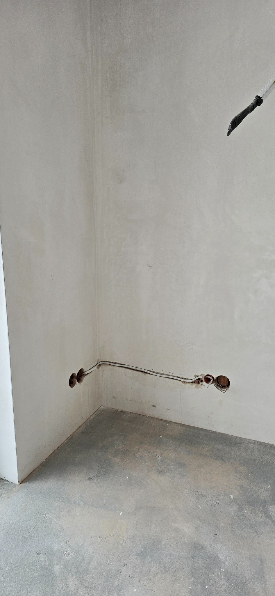 Fragment wnętrza w trakcie prac: przewody elektryczne wystające ze ściany, przygotowane otwory pod gniazdka. Widoczne ślady po kuciu w ścianie.