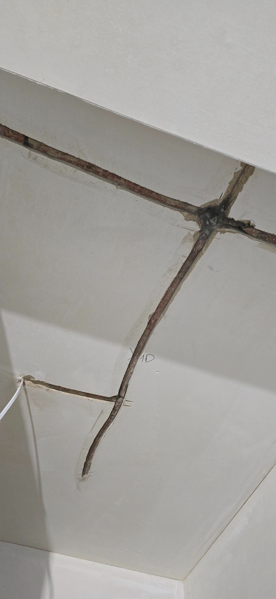 Fragment sufitu z widocznymi, częściowo zamaskowanymi przewodami elektrycznymi w bruzdach. Widoczne ślady po modyfikacji instalacji. Ujęcie z dołu.