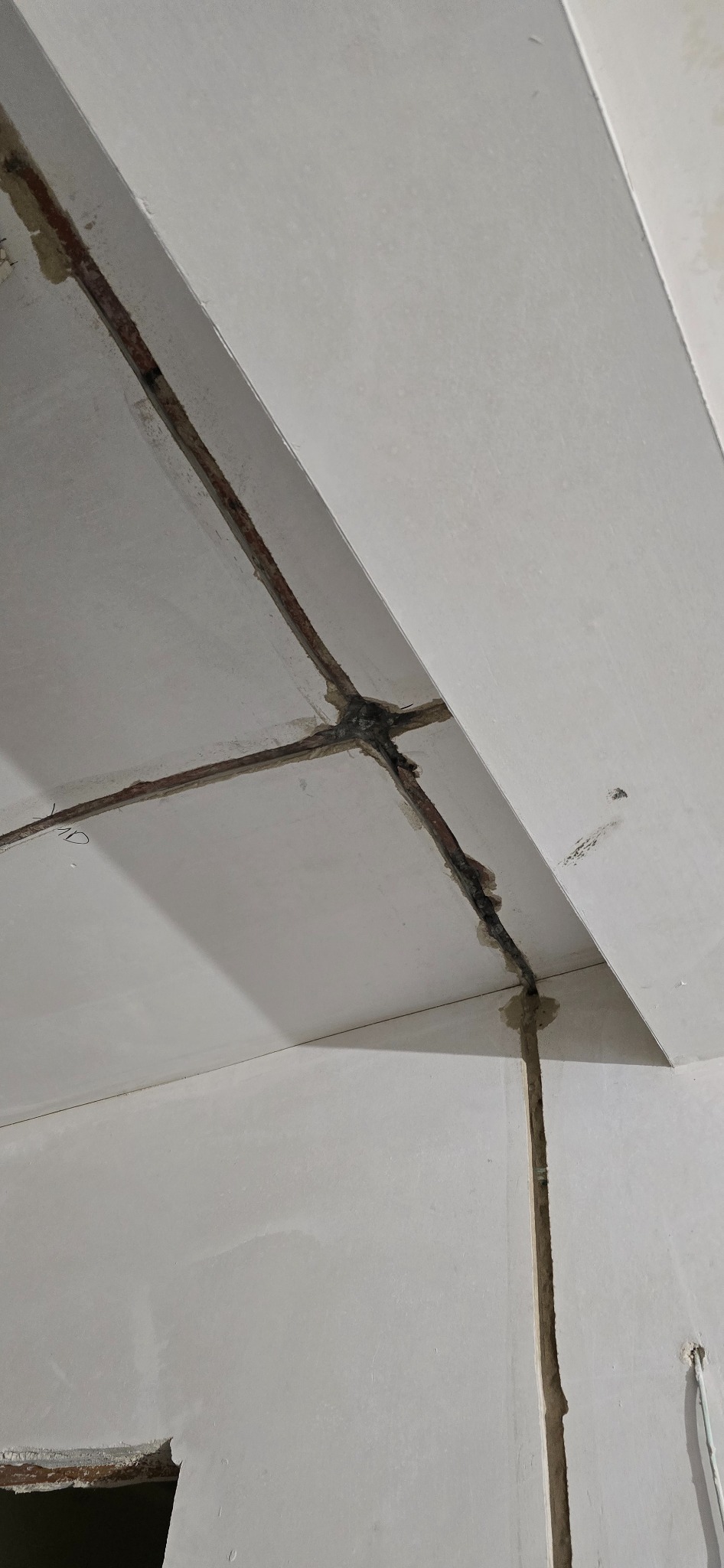 Bruzdowanie pod kable w suficie i ścianie, widoczne kable w szarym tynku. Prace przygotowawcze do instalacji elektrycznej wewnątrz budynku.