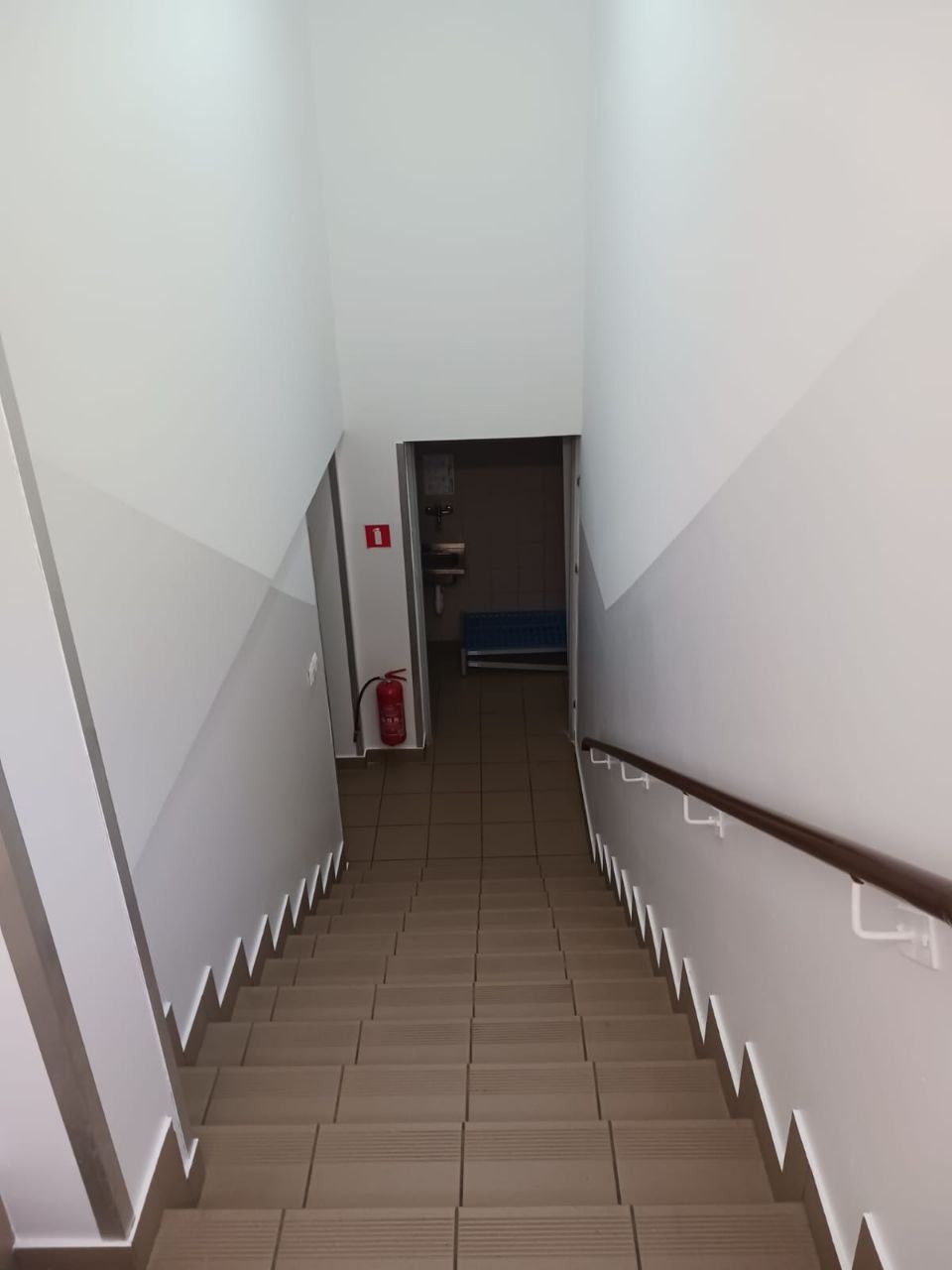 Klatka schodowa po odświeżeniu we Wrocławiu. Ściany pomalowane na biało z szarym pasem na dole. Widoczny brązowy poręcz i gaśnica.