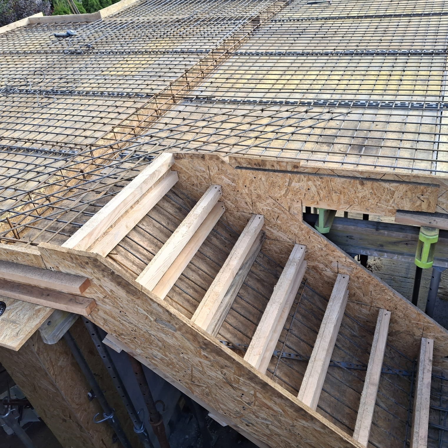 Zbrojenie stropu z drewnianym szalunkiem schodów na budowie domu jednorodzinnego. Widoczne pręty zbrojeniowe i deski szalunkowe. Ujęcie z góry.