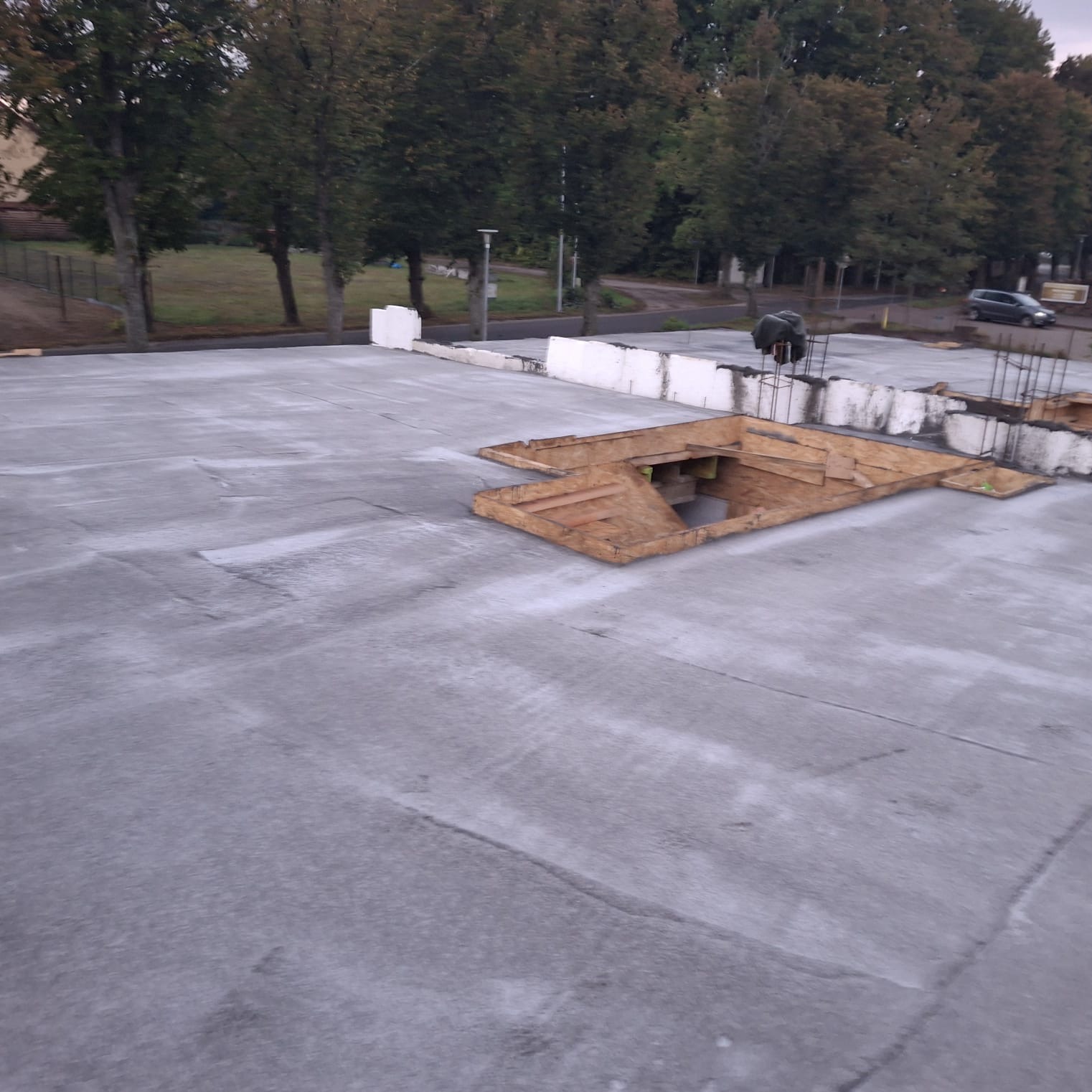 Wylany beton na budowie w Gdańsku. Widoczne szalunki i zbrojenia. W tle drzewa i budynki. Etap prac fundamentowych.