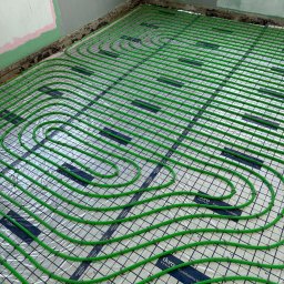 F.H.U.HYDRONOVA Adam Huchmacz - Zielone rury ogrzewania podłogowego ułożone na folii z nadrukiem siatki i logo 'duro system' w surowym wnętrzu przed wylewką. Widok z góry.