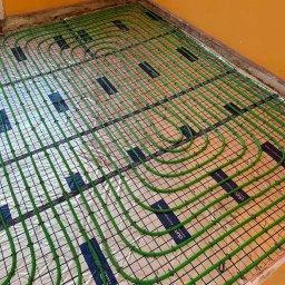 F.H.U.HYDRONOVA Adam Huchmacz - Ogrzewanie podłogowe z zielonych rur na folii aluminiowej, ułożone w pętle na podłodze w Kazimierzy Wielkiej. Widok z góry, żółte ściany w tle.