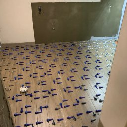 Volodymyr Trufen - Układanie płytek podłogowych w łazience z użyciem systemu poziomowania. Widoczne krzyżyki dystansowe i kliny. Ściany częściowo przygotowane pod wykończenie.