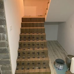 Volodymyr Trufen - Schody w trakcie układania płytek imitujących drewno, z użyciem krzyżyków dystansowych. Widoczne wiaderka z zaprawą i fragment ściany z surowego betonu.