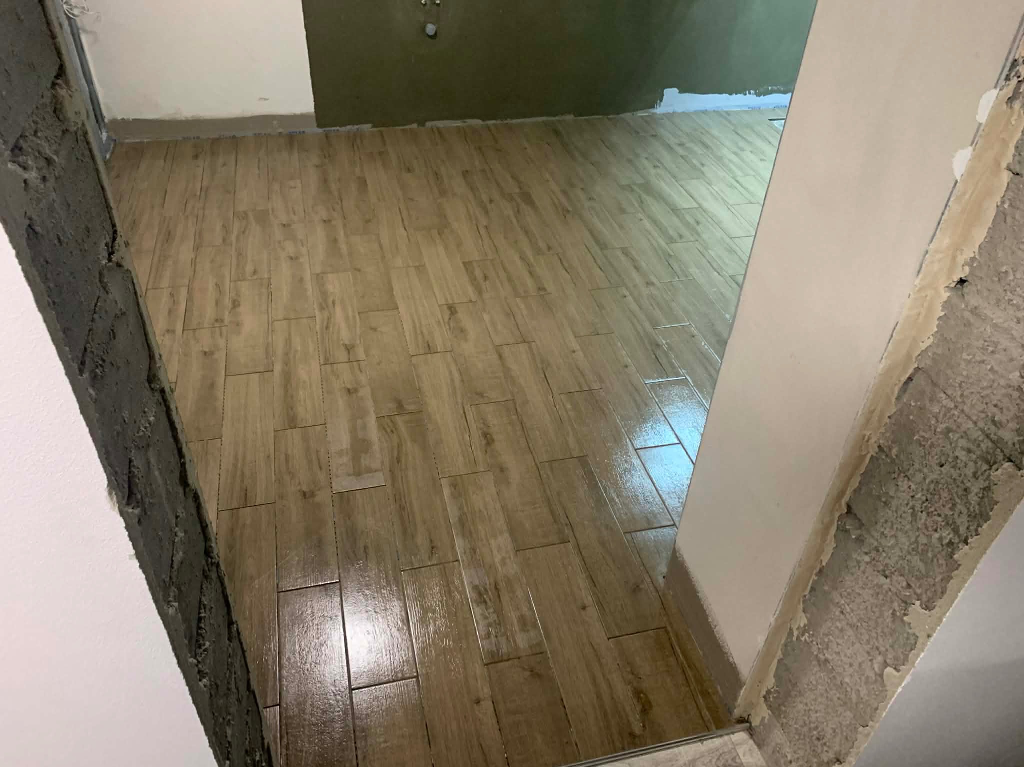 Ułożona podłoga z płytek imitujących drewno w trakcie wykańczania, widoczne surowe ściany i przygotowane do malowania. Jasne płytki ułożone w jodełkę.